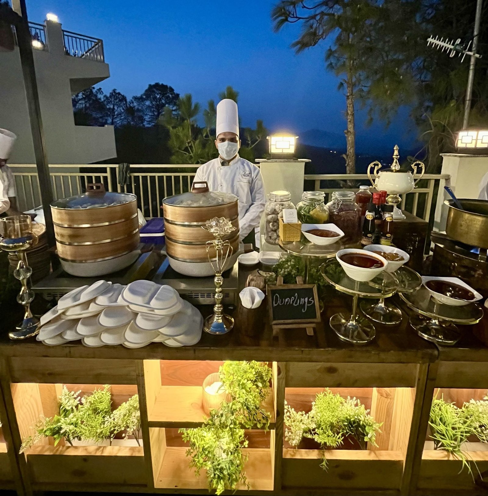 A live dumpling counter at blue hour, bamboo steamers, sauce bowls and a chalkboard sign